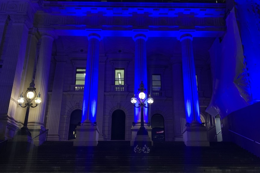 Victorian Parliament is illuminated in blue light on the outside, a photograph taken looking up the steps shows.
