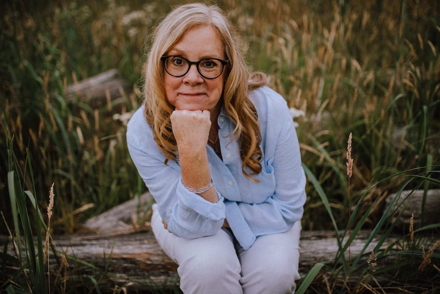 A middle-aged woman in glasses and shirt in a grassy field