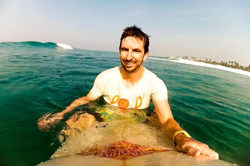 A man wearing a white shirt on a surfboard in the ocean