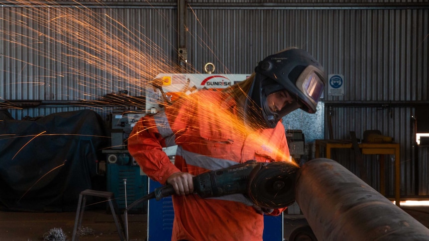 Woman in High-vis and helmet grinding metal with sparks flying