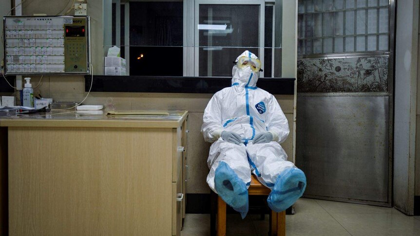 A medical worker in protective suit sits on a chair to take a break