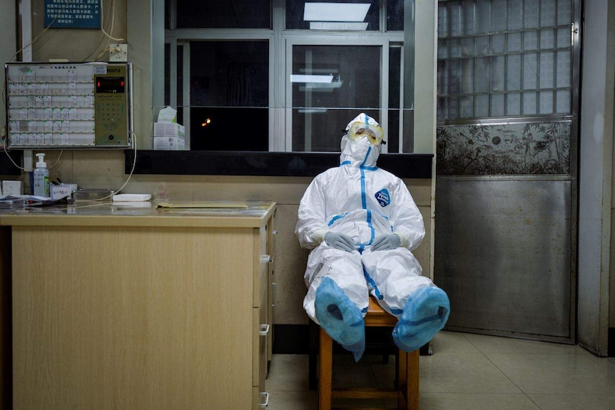 A medical worker in protective suit sits on a chair to take a break