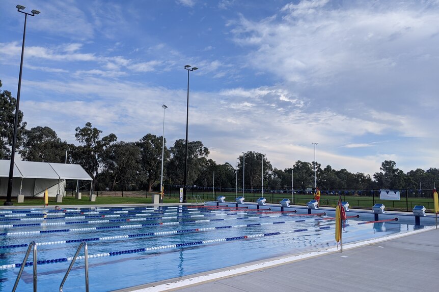 A swimming pool under a blue sky, a lifeguard standing at one end. 