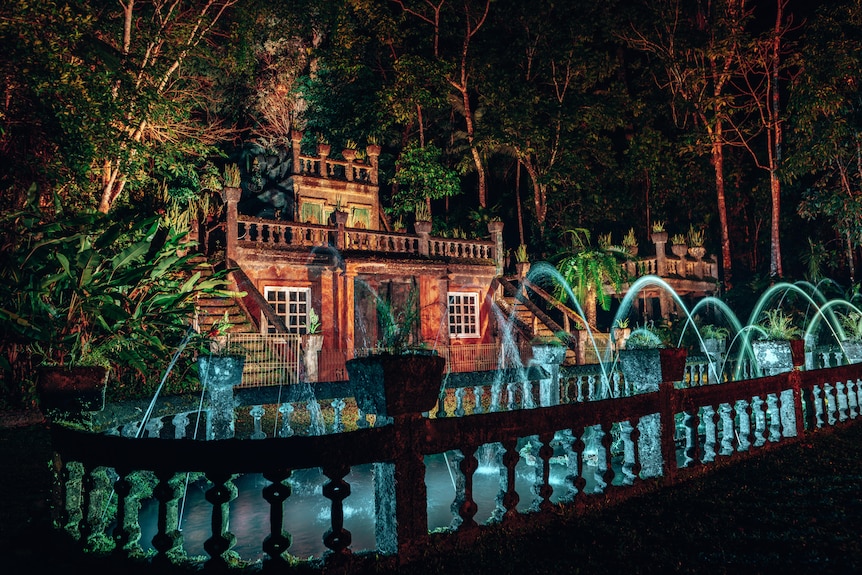 A photo of castle with an active water feature, lit up by flood lights at night.