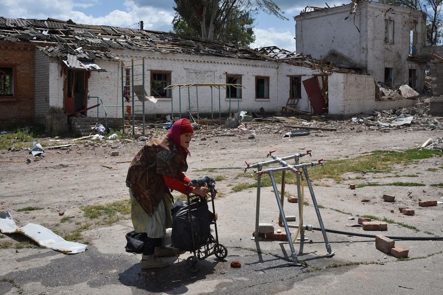 An elderly woman stands next to buildings destroyed in the Russian strike.