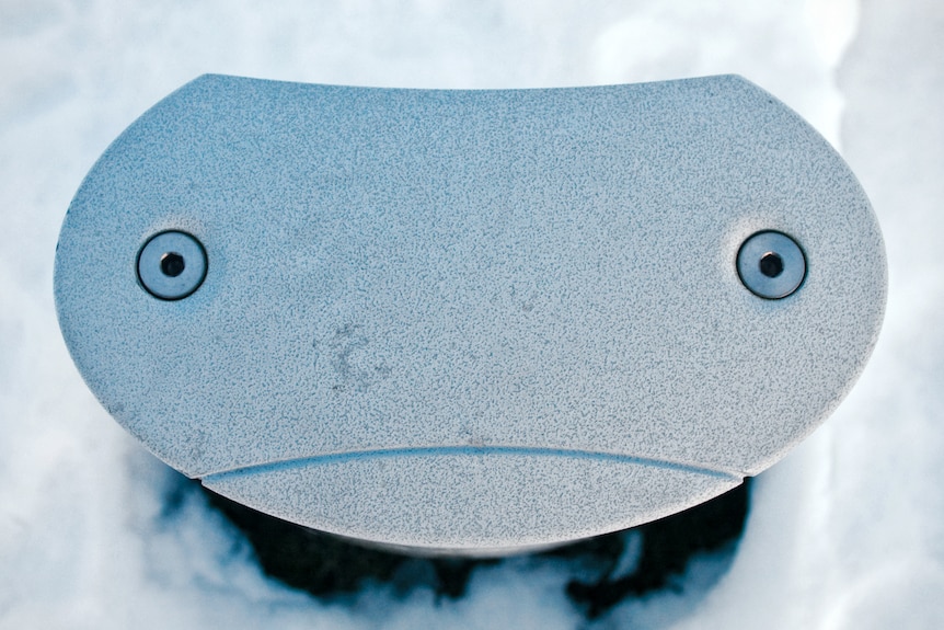 A light poking out of snow with patterns that looks like a sad robot face.