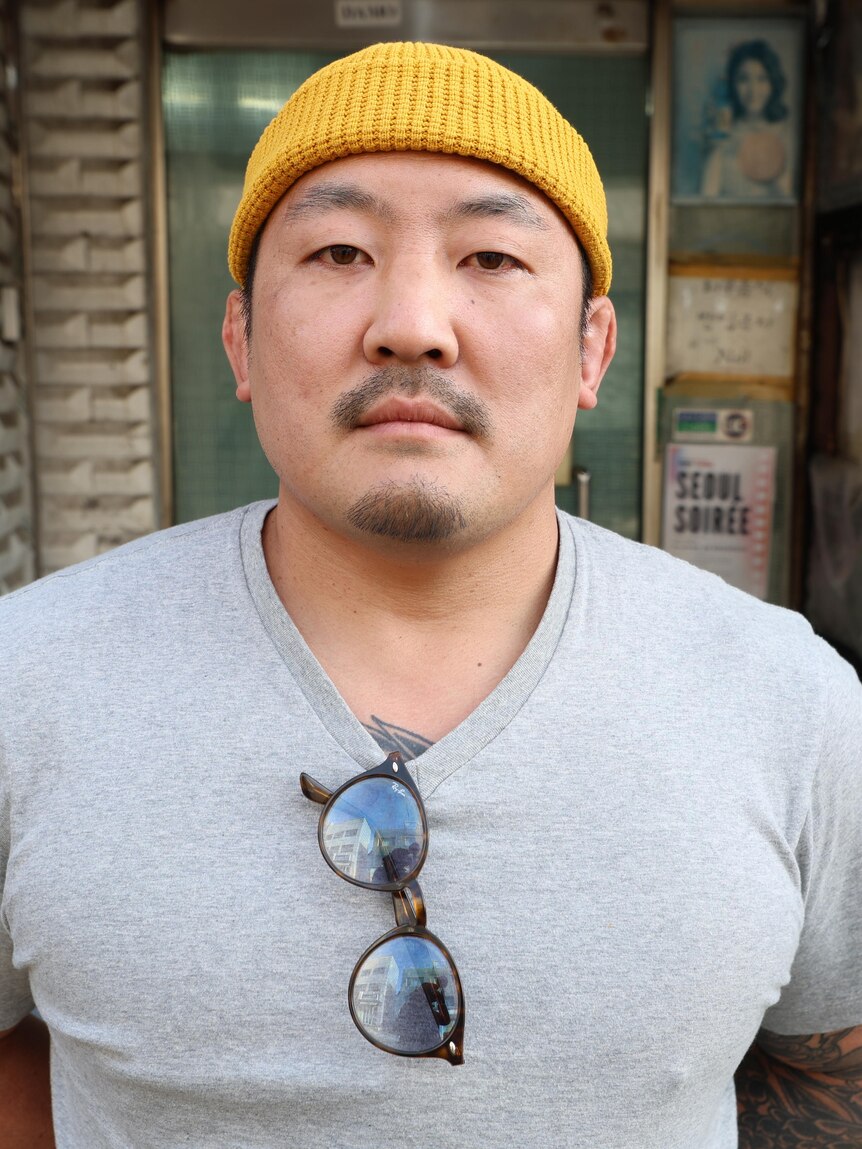 A man wearing a yellow beanie and T-shirt with his sunglasses tucked in the front
