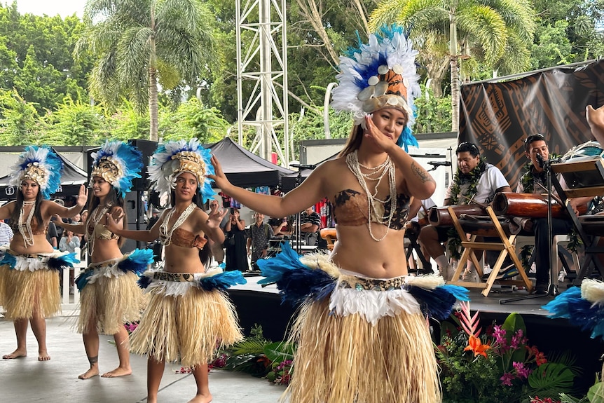 Four women in traditional Cook Islands dress dance infront of stage with traditional drums. 