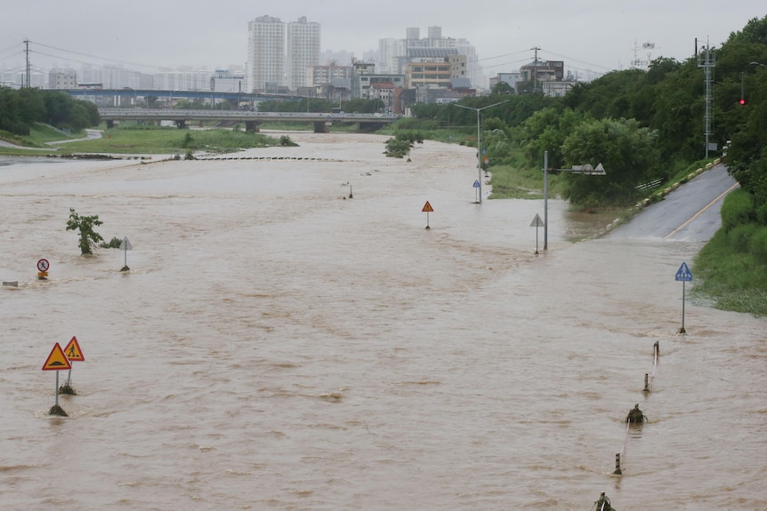A wide image shows extensive flooding blocking a major road while skyscrapers can be seen in the background.