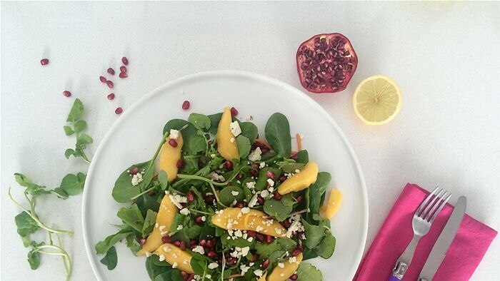 Salad on a plate, with a cut pomegranate and lemon beside it.