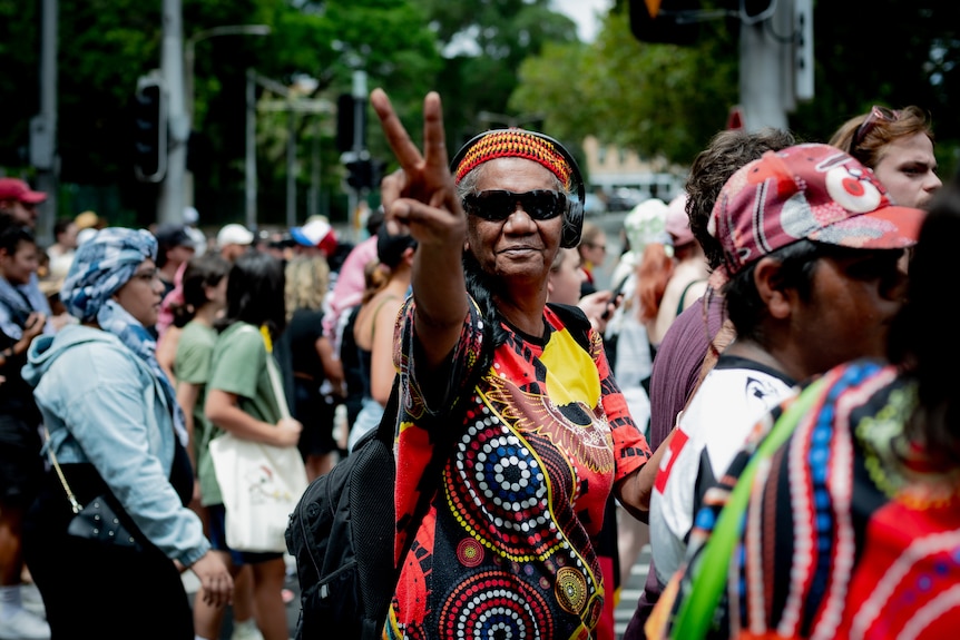 An indigenous woman holds the peace sign up towards the camera.