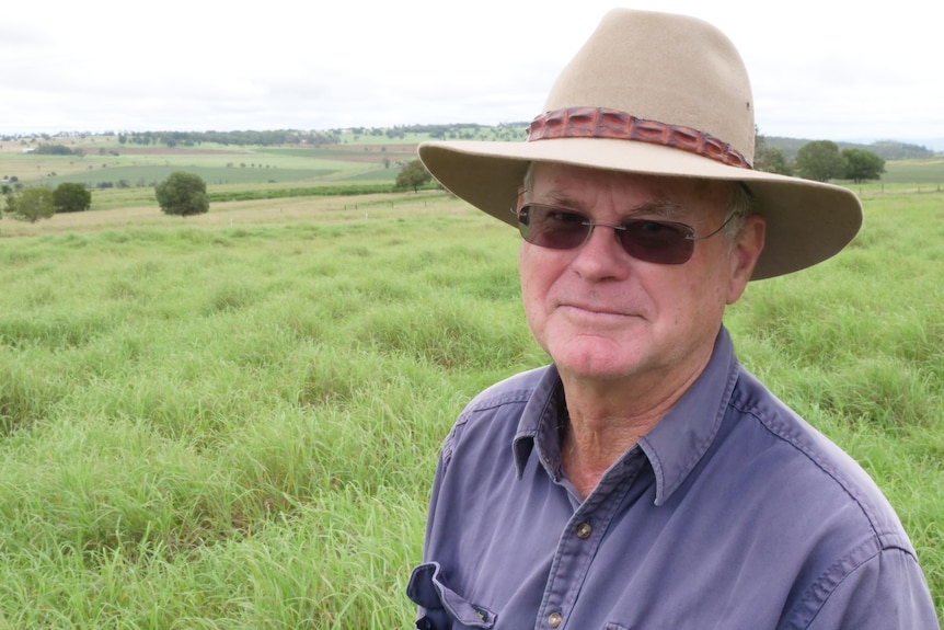 A man wearing a hat standing in front of a paddock of green grass