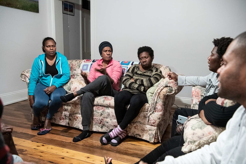 Ellen George sits on a couch between two female housemates, and gestures with her hands us she talks.