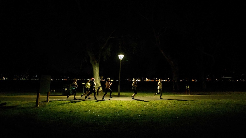 A group of women running in a park under a light post