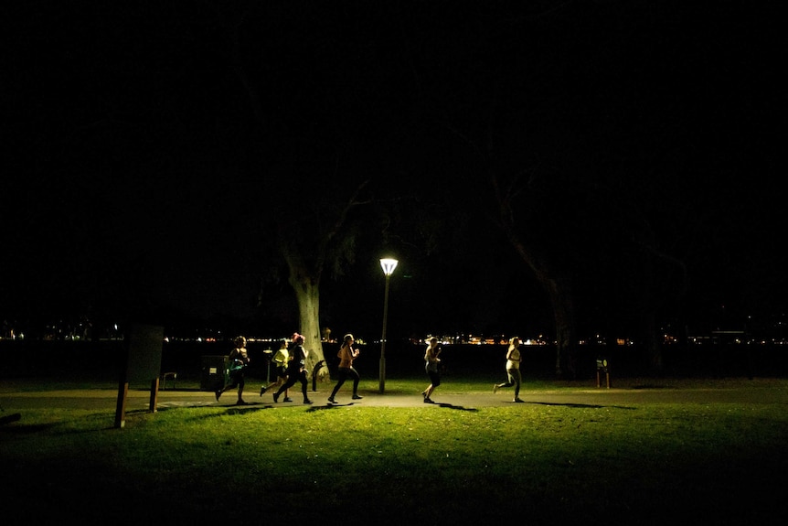 A group of women running in a park under a light post