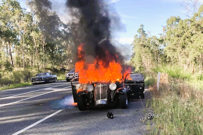 A hot rod on fire on the side of a road.