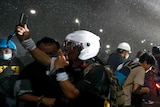 Crowds of people, some wearing helmets, duck away from a spray of water.