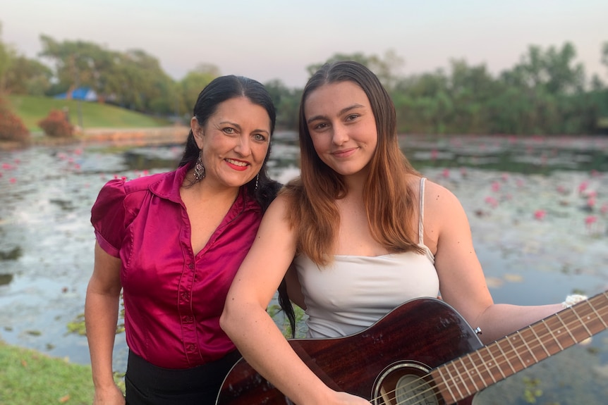 Daughter with guitar with mum at a suburban lake setting. Smiling.