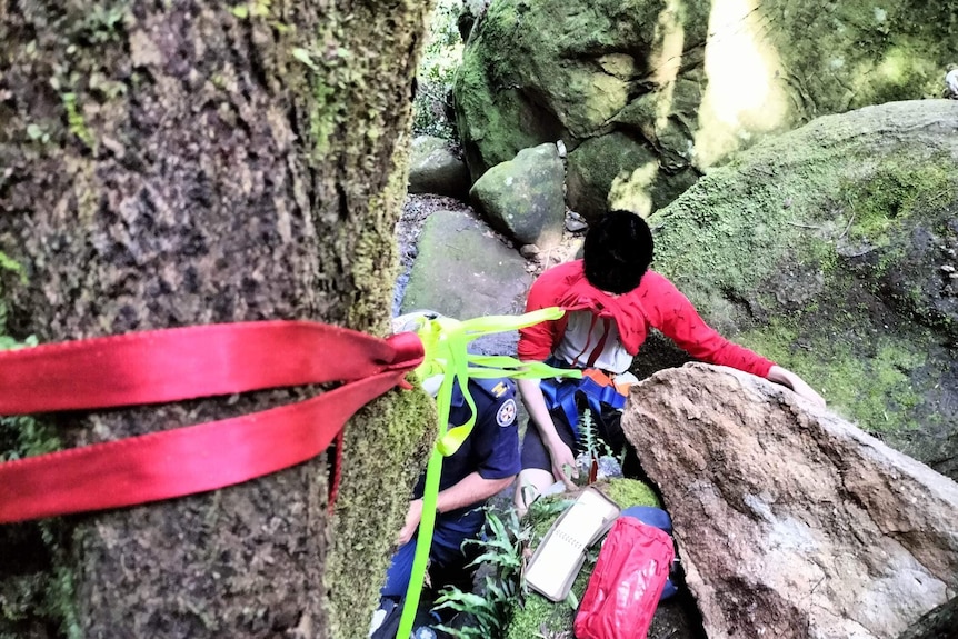 a man trapped by a boulder is assisted  by emergency personnel