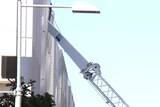 The top portion of a truck crane that toppled over rests inside the top of a building.
