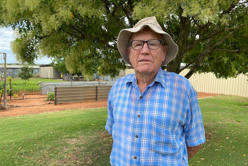 A man looking at the camera wearing a hat, glasses and blue checked shirt.