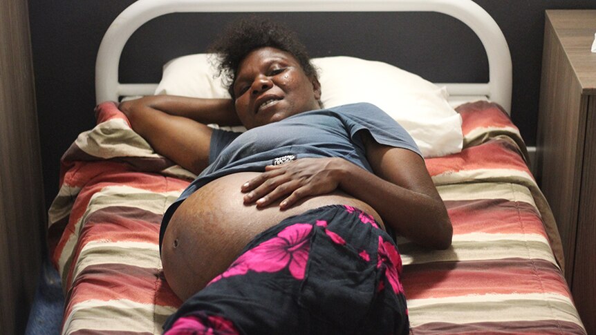 A pregnant woman in bed holding her stomach
