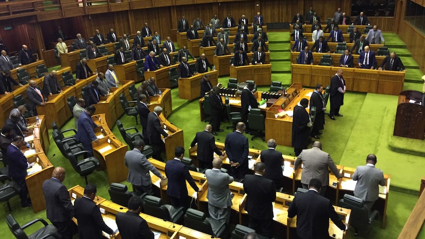 Men in suits stand in a semi-circle on the lime-green floor of Parliament.