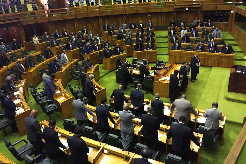 Men in suits stand in a semi-circle on the lime-green floor of Parliament.