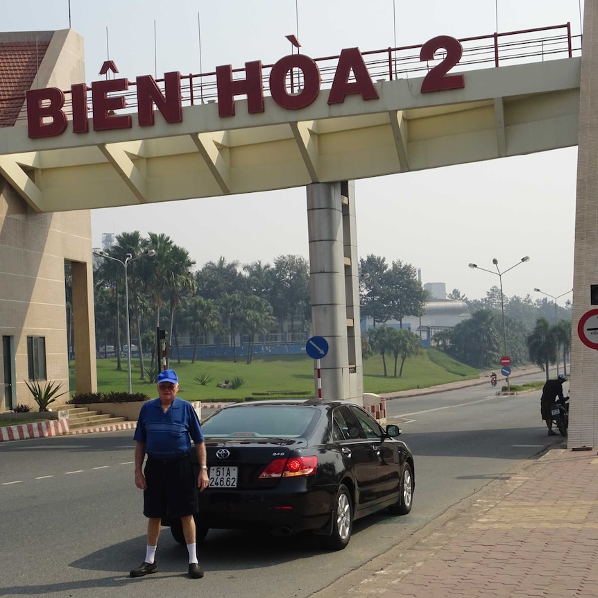 Man stands beside black car under a bridge with Vietnamese writing on it