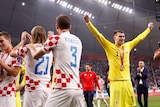 A man in a yellow goal keeper jersey with a medal with arms raised, next to men in white and red jerseys clapping