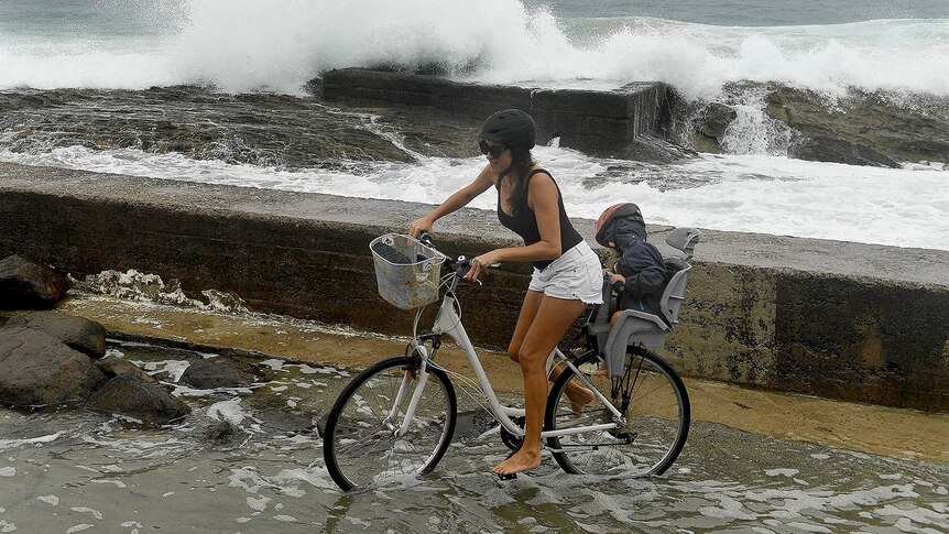 A woman on a bicycle and a small child negotiates a flooded path at Snapper Rocks on the Gold Coast.