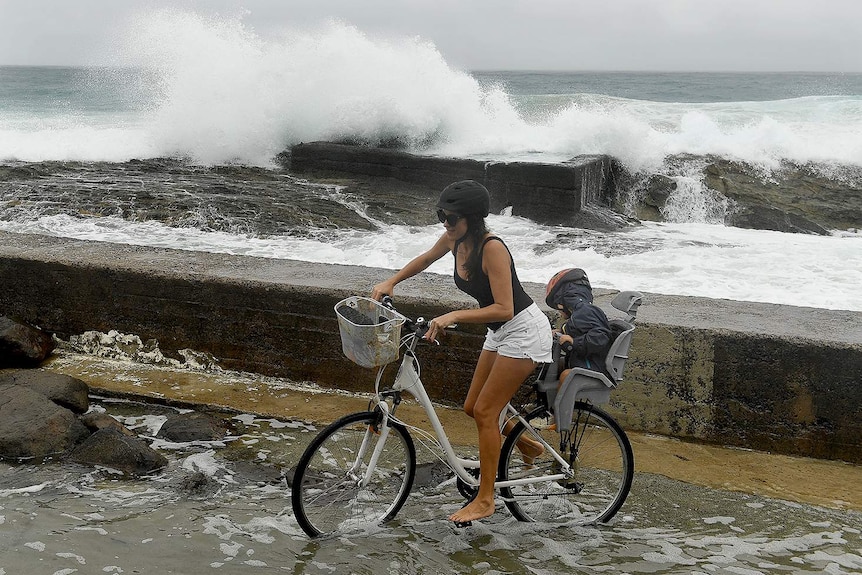 A woman on a bicycle and a small child negotiates a flooded path at Snapper Rocks on the Gold Coast.