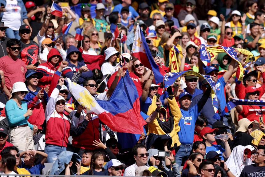 A crowd shot of Philippines fans in the crowd, waving a flag and standing to cheer.