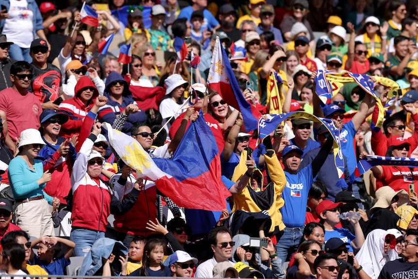 A crowd shot of Philippines fans in the crowd, waving a flag and standing to cheer.