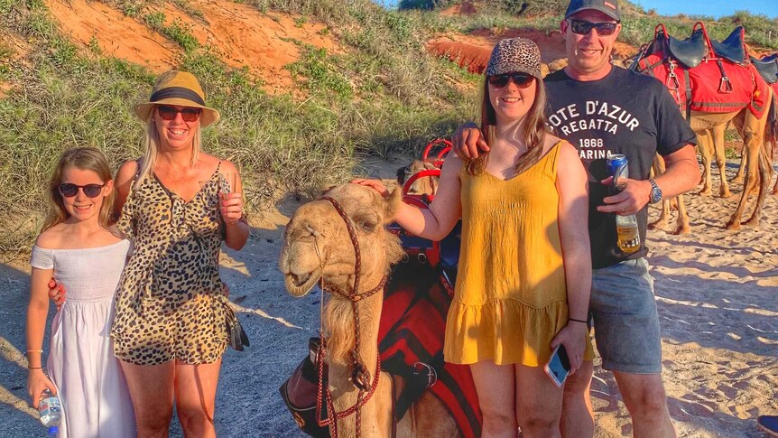A family of four pose with a camel with drinks in their hands.