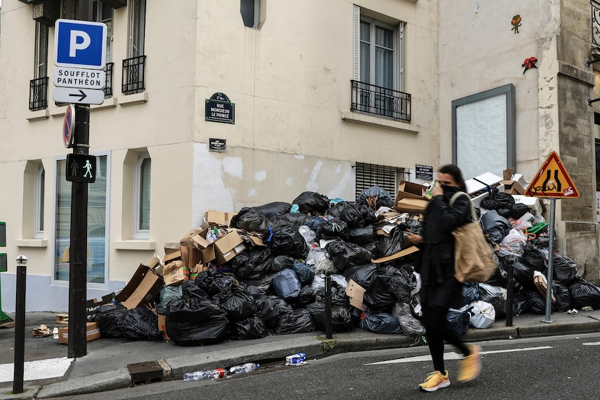 A woman covers her face as she walks past a large pile of rubbish.