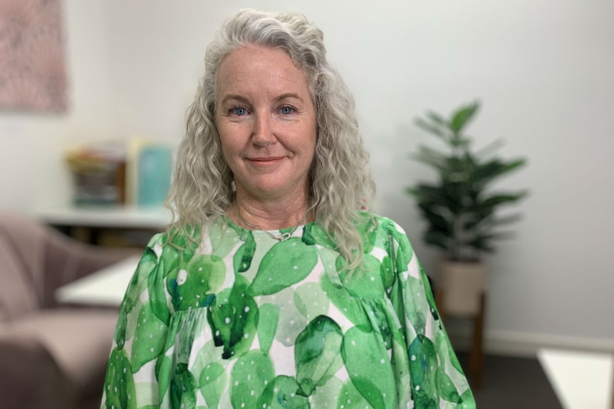 A woman with a green top and grey hair smiles warmly at the camera.