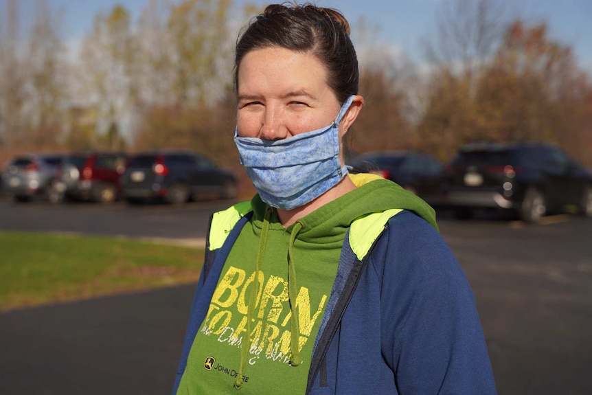 a woman with a blue face mask outside looks at the camera