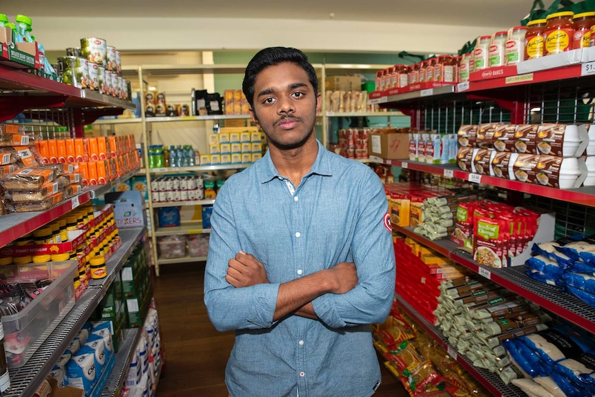 A man stands in a supermarket aisle looking at the camera