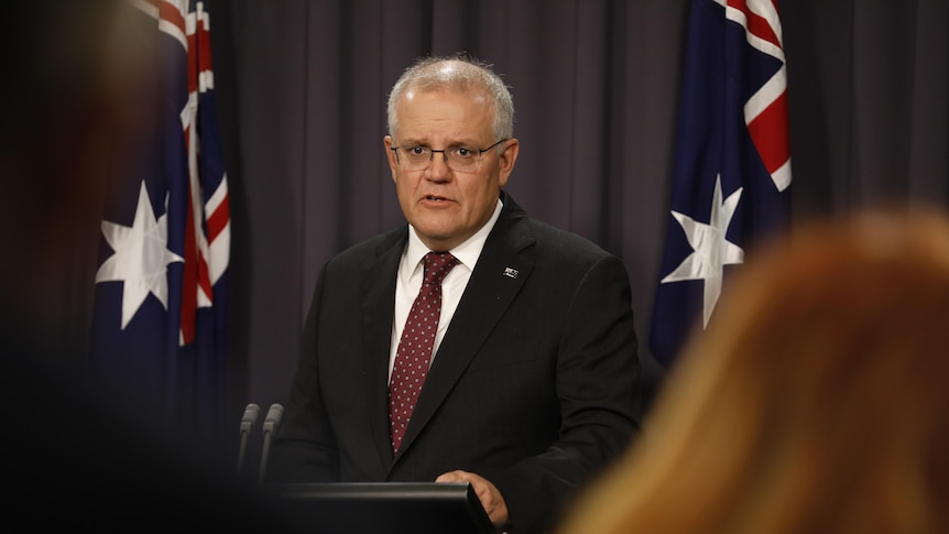 Prime Minister Scott Morrison speaking in front of a lectrern with two Australian flags behind him.