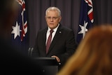 Prime Minister Scott Morrison speaking in front of a lectrern with two Australian flags behind him.