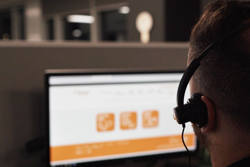 A man with a headset on stares at a computer.