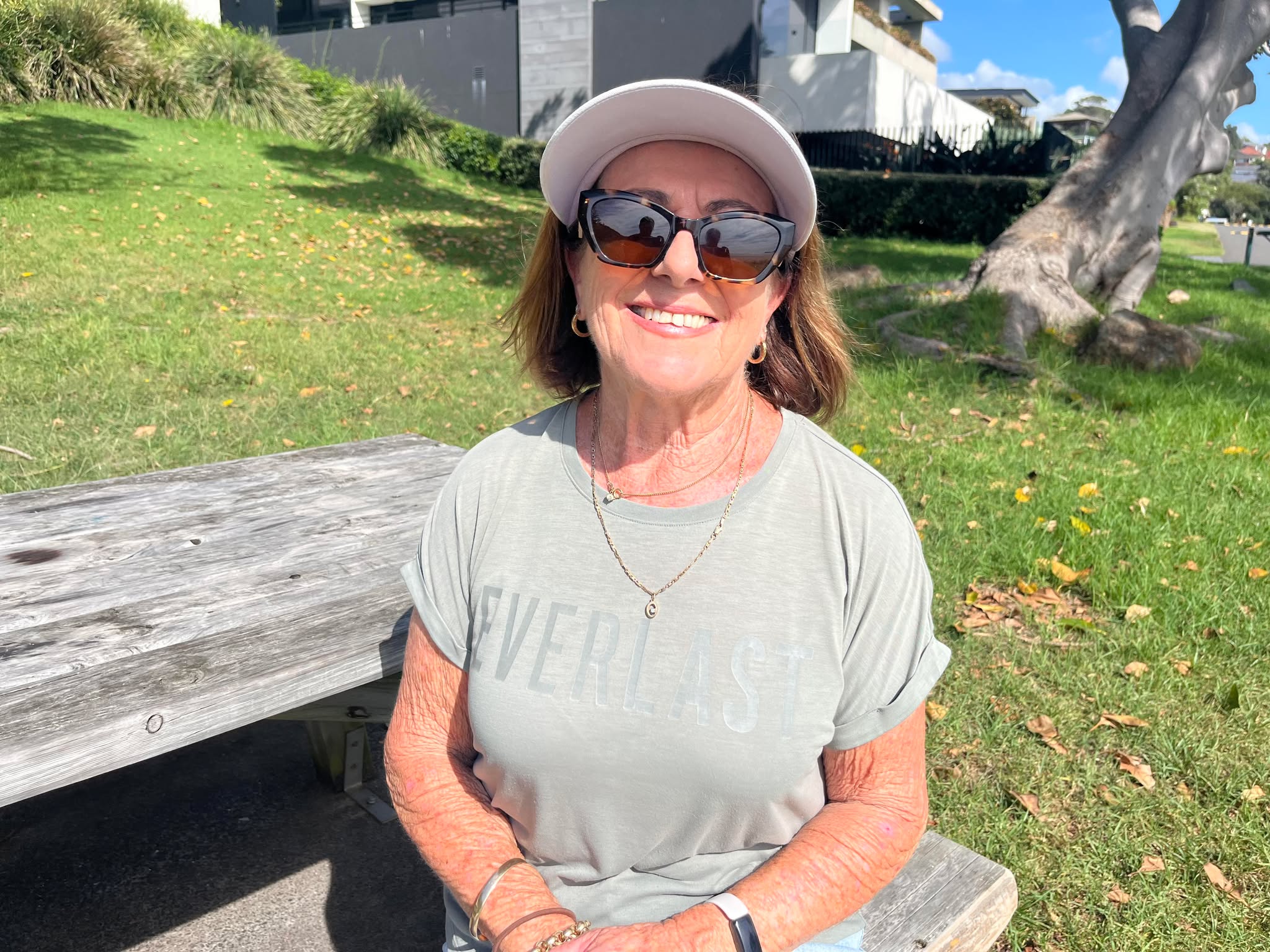 Brunette woman with glasses, hat, smiling on beach park bank