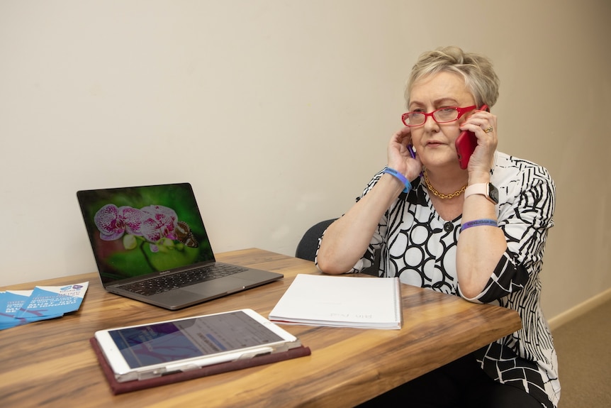 A gray-haired woman sits at a desk and talks on the phone