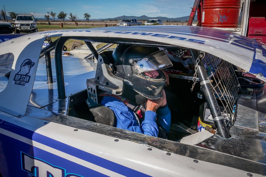 A race car driver puts on his helmet in a speedway car
