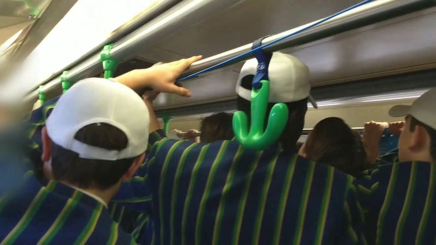 A still frame of a video shows a group of boys in private school blazers, seen from the back, filling a crowded tram.