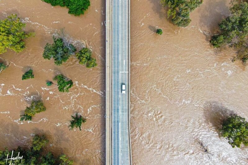 An aerial view of a car driving over a bridge surrounded by floodwater.