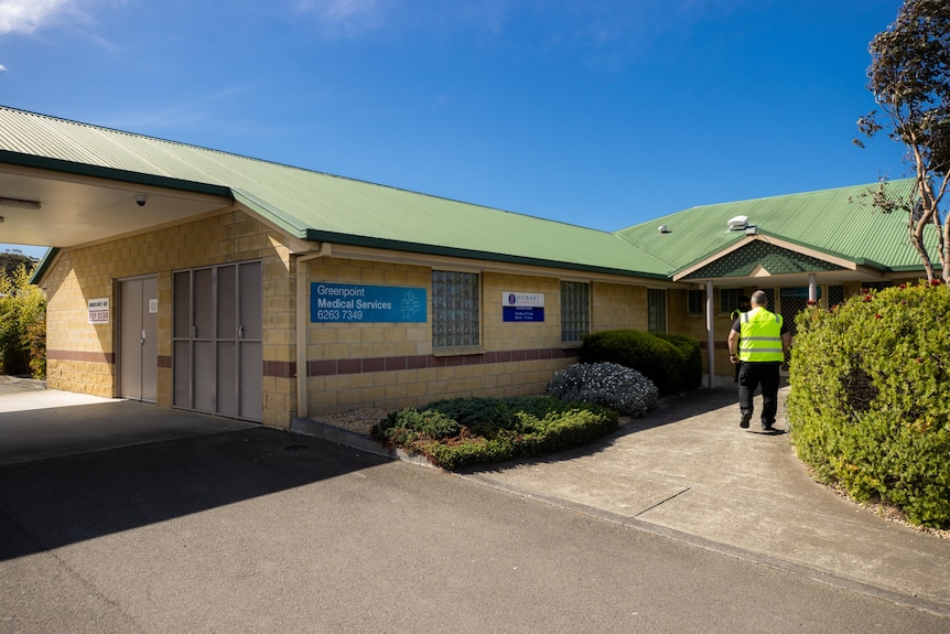 A single-storey medical clinic building with a man in a high-vis vest walking in the entrance.