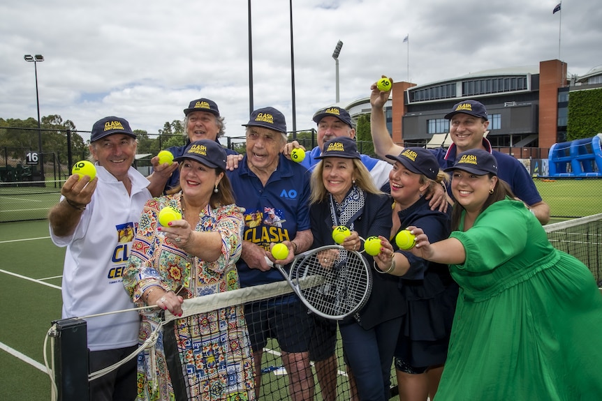 People gathered together holding tennis balls on a green tennis court