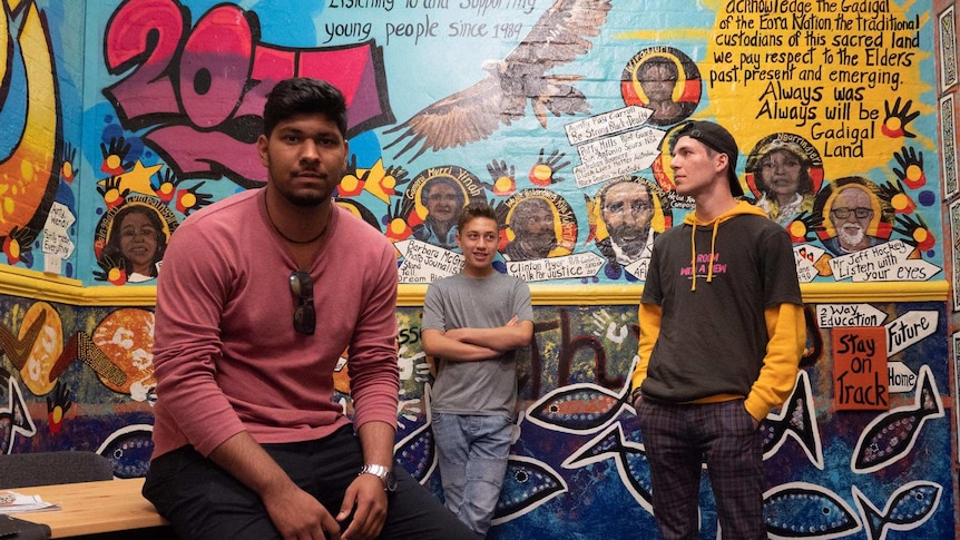 Three students stand in front of a mural at the Glebe Youth Service